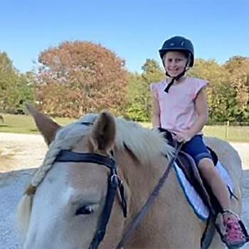 child wearing a helmet while riding a horse