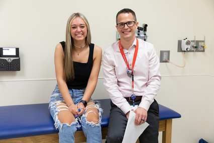 Teen patient and health care provider seated together on an exam table in a clinic room during an outpatient medical visit