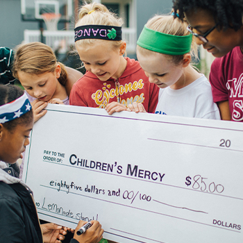 Group of children presenting a ceremonial donation check to Children's Mercy while participating in a fundraising activity.