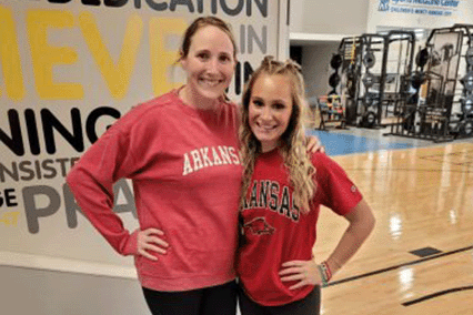 Two people standing together in an indoor sports medicine or rehabilitation facility, posing for a photo with exercise equipment and training space visible in the background.