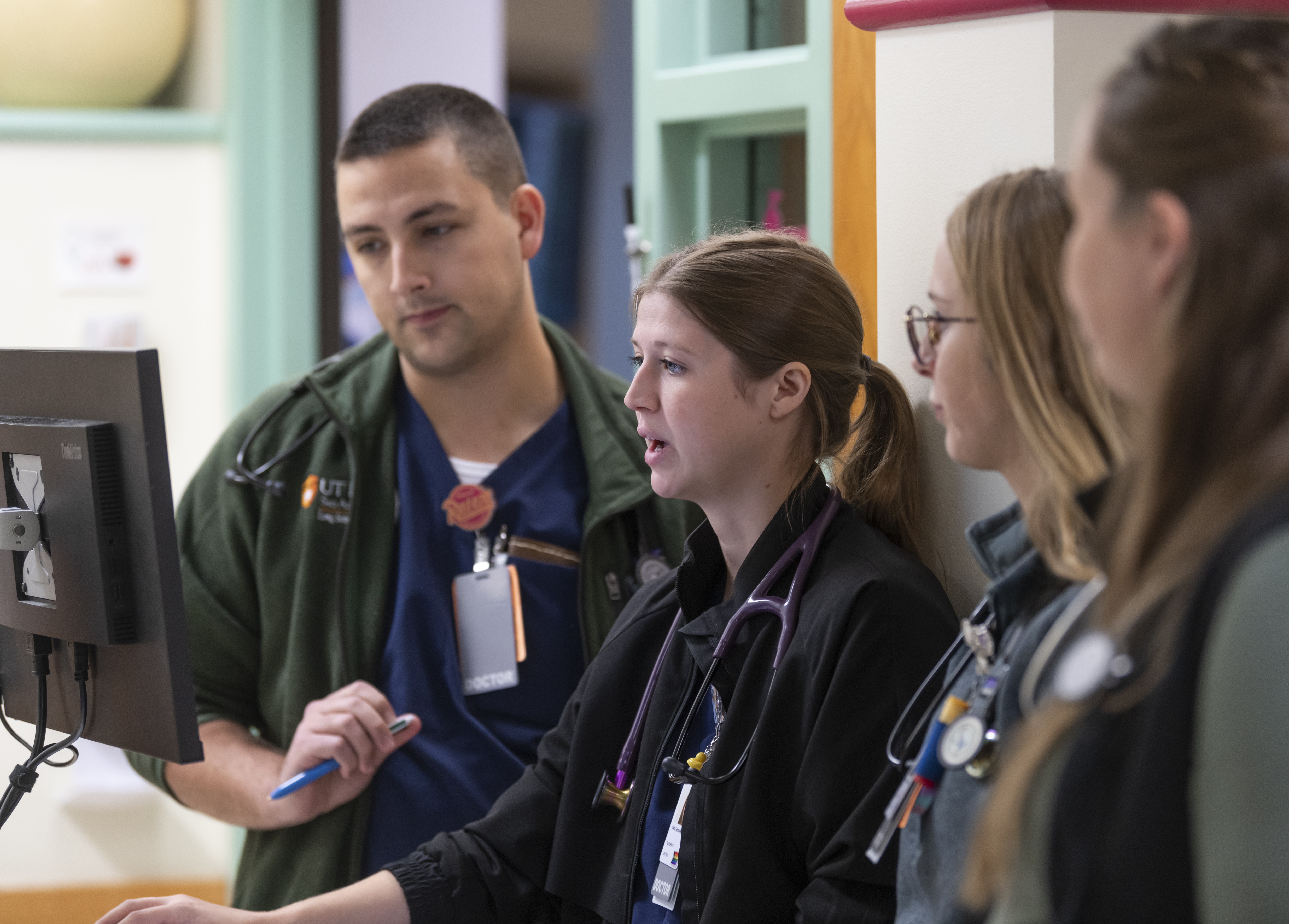 Four clinicians review information on a computer workstation in a hospital unit, collaborating during patient care rounds.