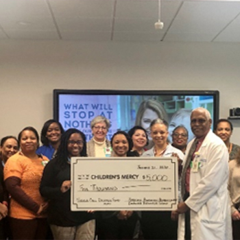 "Hospital team members posing with a ceremonial donation check for Children's Mercy in front of a display screen during a fundraising or recognition event."