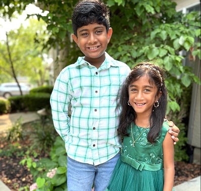 Two children standing together outdoors in a garden setting.