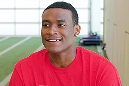 Portrait of a person wearing a red shirt, seated in an indoor athletic training facility