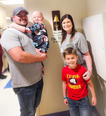 Two adults and two children posing together in a hospital hallway, with one adult holding a child.
