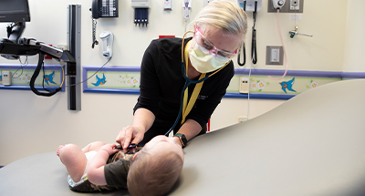 Health care provider listening to an infant's heartbeat with a stethoscope during a pediatric exam in a clinic room