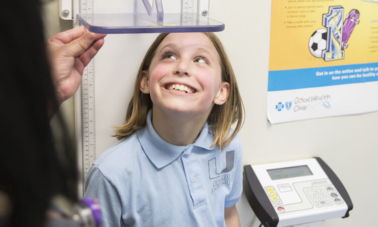 Child having height measured with a stadiometer during a pediatric clinic visit while a health care provider adjusts the measuring bar.