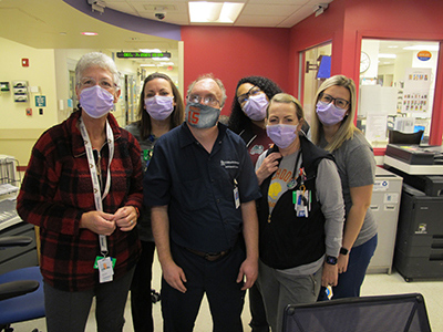 Group of six hospital team members wearing face masks and standing together in a clinical work area.