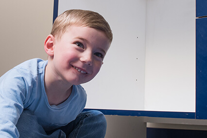 Young child crouching beside a play structure or activity area indoors, looking toward the camera.