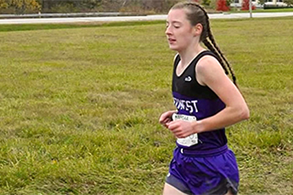 Youth runner participating in a cross-country race while running across a grassy course.
