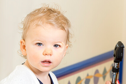 Close-up of a young child holding an otoscope in a pediatric exam room during a clinic visit.