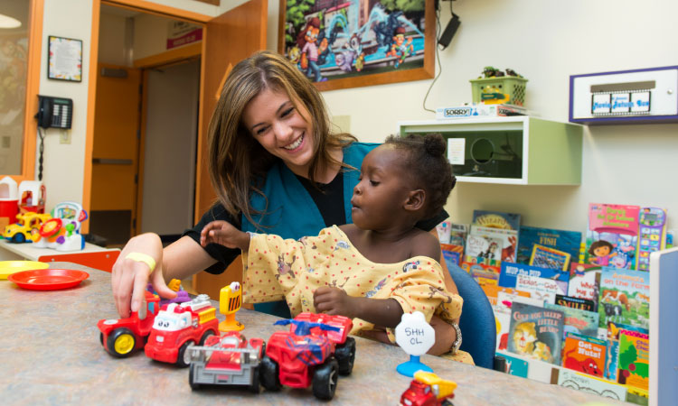 Health care team member and child playing with toy vehicles during a pediatric activity session in a hospital playroom or child life setting.