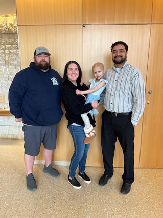 a mom holds child and poses with dad and a clinician