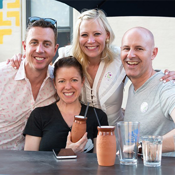 Four adults seated together at an outdoor table, posing for a group photo 