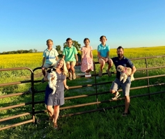 photo of family of six near a fence on a farm with their two dogs