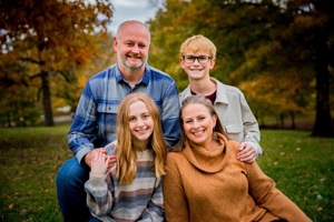 photo of family of four posing for a family photo outside with green grass behind them