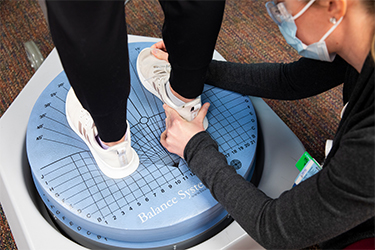 photo of patient wearing white shoes stepping on a blue circle machine for exercises