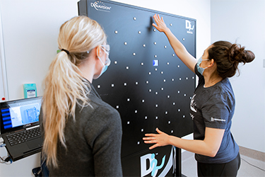 photo of two healthcare team members looking at the wall where a large machine stands flat against the wall