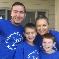 photo of family of four outside of a house, all are wearing blue shirts, all are smiling