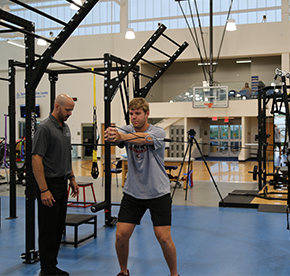 Athlete practicing a movement assessment exercise with guidance from a clinician in a rehabilitation and performance training facility.