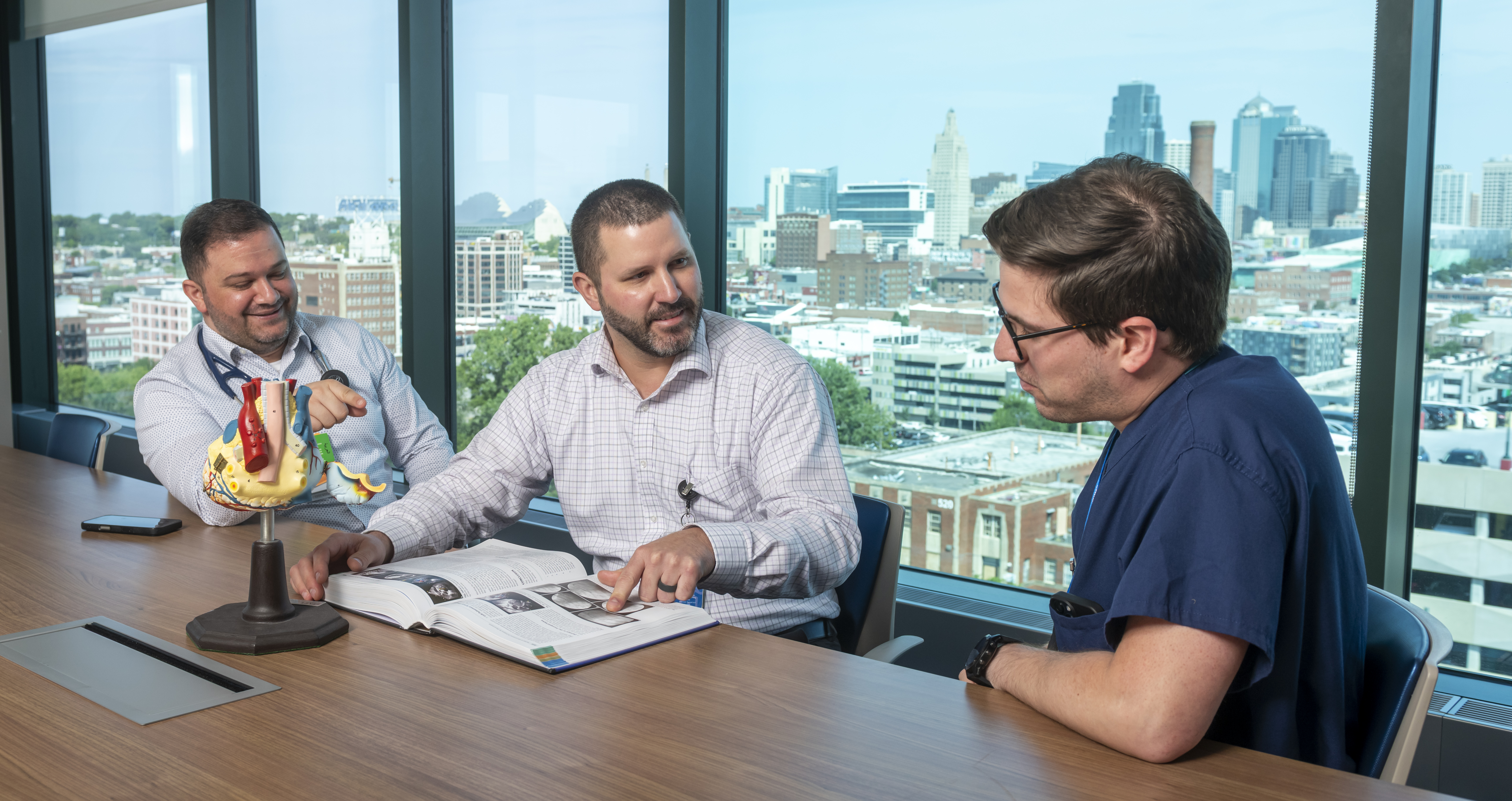 three cardiology fellows and staff look at a book and 3D model of the heart