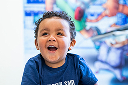 Young child seated indoors in a pediatric setting, with colorful artwork visible in the background.