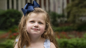 Young child sitting outdoors with a large navy bow in their hair