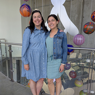 Two adults stand arm in arm at Children’s Mercy, with suspended glass sculptures visible in the background.
