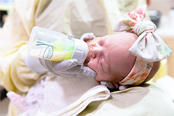 Infant being bottle-fed by a caregiver during a pediatric visit.
