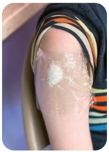 Close-up of a child's upper arm with a bandage covering an injection site.
