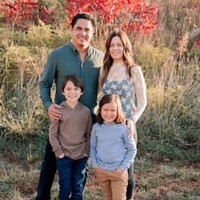 A women posing outdoors with her husband and two kids. All but one wearing denim and youngest child to the right wearing Kakis. 