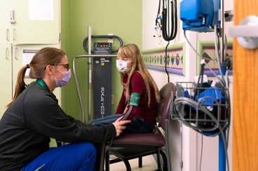 a photo of a nurse checking vital signs of a patient sitting in a chair