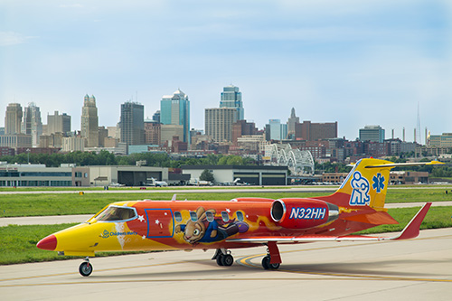 Children's Mercy Lear jet aircraft on an airport taxiway with the Kansas City skyline in the background.