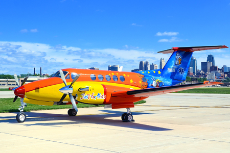 Colorfully painted Children's Mercy turbo prop aircraft parked on an airport runway.