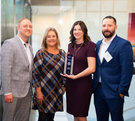 Four people in business wear stand together, smiling and holding a trophy that features the Center for Disability Inclusion logo and reads: “Children’s Mercy Kansas City: In recognition of outstanding achievement for 2024 Leader in Disability Inclusion.”  