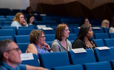 Attendees seated in an auditorium listen during a presentation.