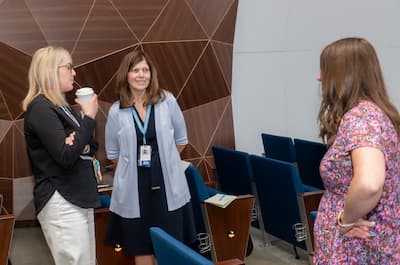 Three attendees chat in an auditorium between sessions.