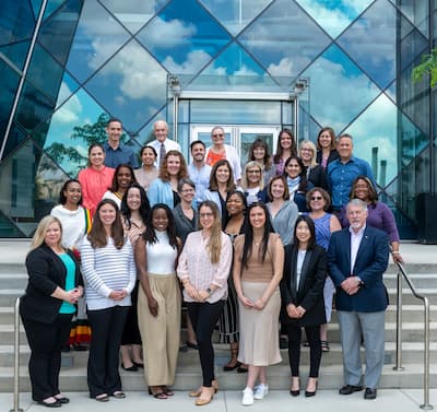 Group of Children's Mercy team members standing on outdoor steps in front of a glass building entrance for a team photo.