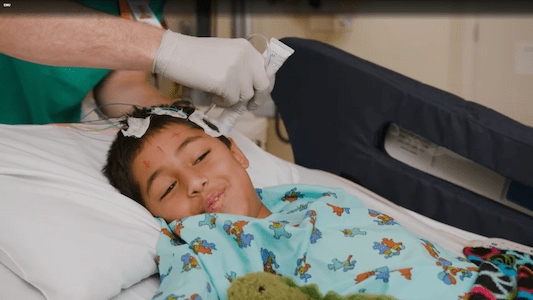 Health care team member adjusting monitoring electrodes on a child’s head while the child rests in a hospital bed