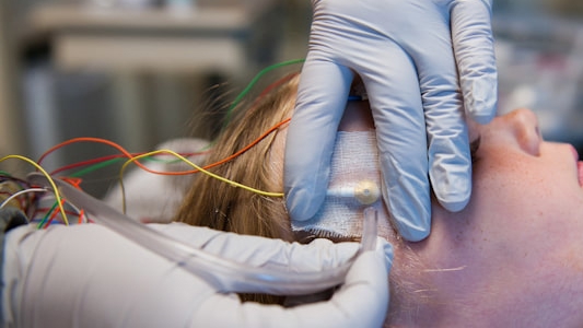 Gloved hands placing an electrode and lead wires on a patient's head as part of a procedure