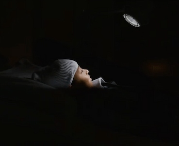 Child resting in a hospital bed wearing a neurological monitoring cap while being observed in a dimly lit room