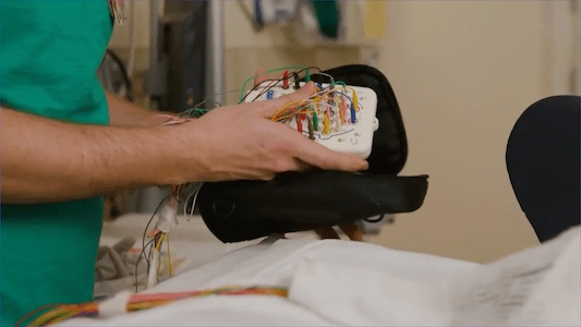 Health care team member holding a diagnostic monitoring device connected to multiple electrode wires
