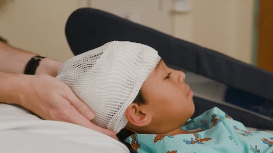 Child lying in a hospital bed with a mesh cap securing diagnostic monitoring sensors during a medical assessment