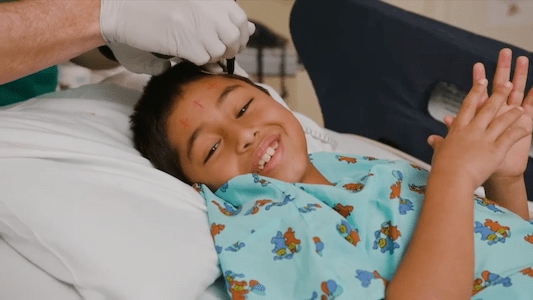 Child resting in a hospital bed while a health care team member examines their head