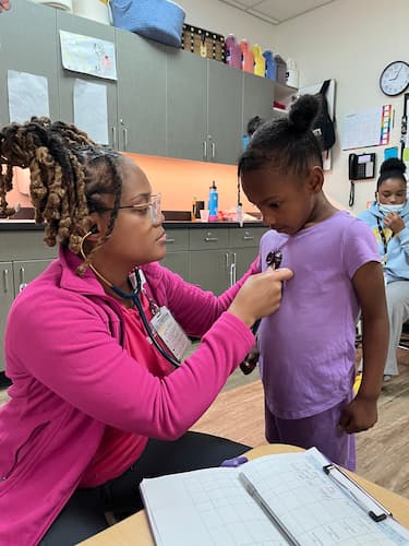 A female health care professional listens to a child's chest with a stethoscope during a clinic exam.