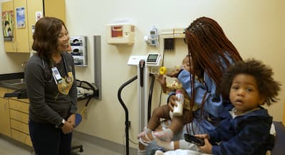 Child and caregiver meeting with a health care team member in an exam room