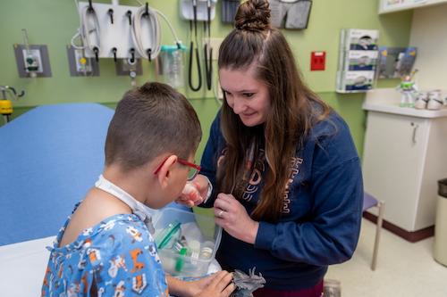 Child Life specialist demonstrating a breathing treatment mask to a child in a clinic exam room