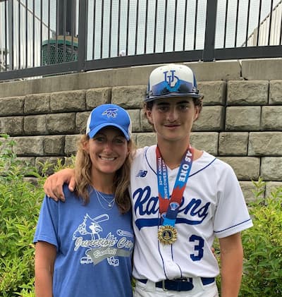 Person wearing a baseball uniform and medal posing for a photo with another person outdoors after a baseball event