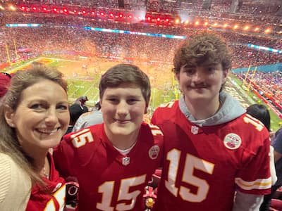 Three people at a football stadium, with two wearing red Kansas City Chiefs number 15 jerseys and the field visible in the background.