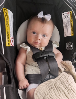 Infant seated in a child safety seat with a blanket and bow headband